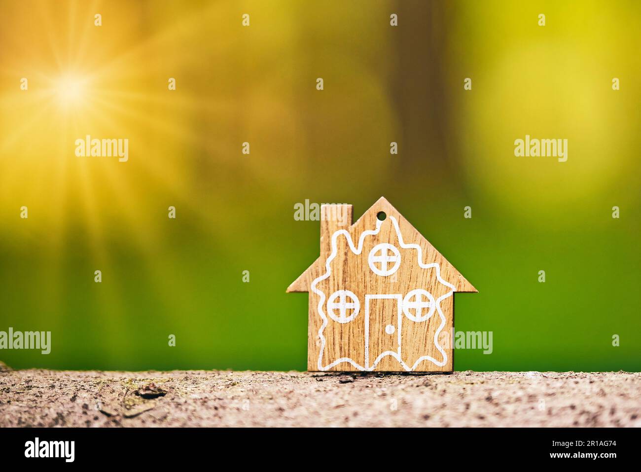 Primo piano del modello di casa in legno su sfondo verde foresta con sunflare. Casa ecologica e concetto di sostenibilità. Spazio di copia. Messa a fuoco selettiva. Foto Stock