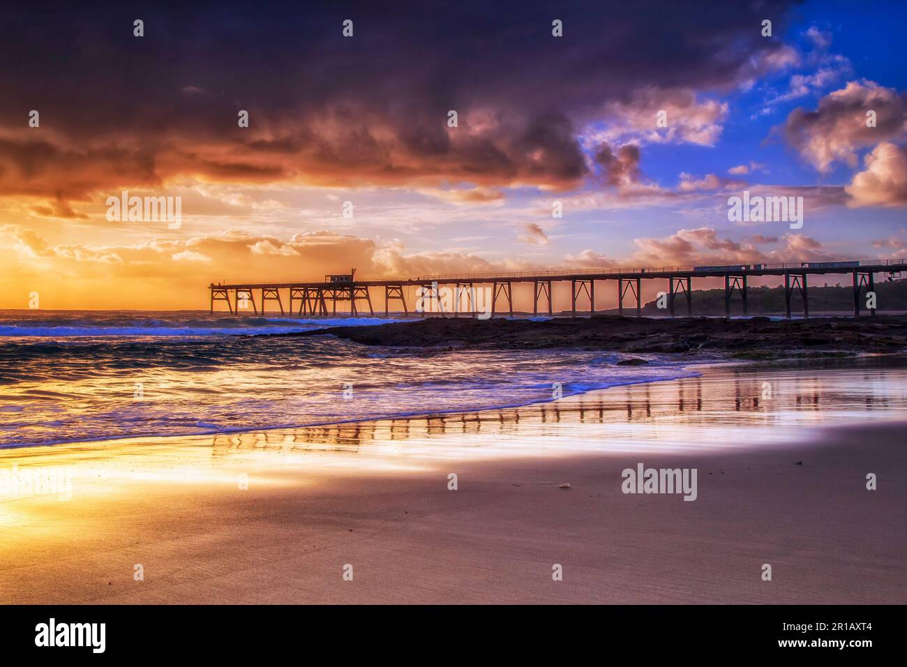 Lontana Catherine Hill Bay Spiaggia di mezzo campo storico molo di industria del carbone sulla costa australiana del Pacifico, con il tempo scenico all'alba. Foto Stock