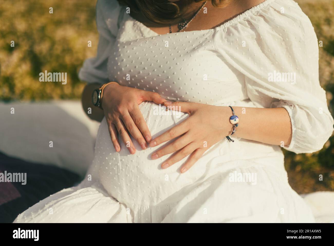 In un primo piano del ventre, una donna incinta forma con le mani un cuore, un'affascinante coccinella appoggiata sulla pelle, simbolo dell'amore e del buon luc Foto Stock