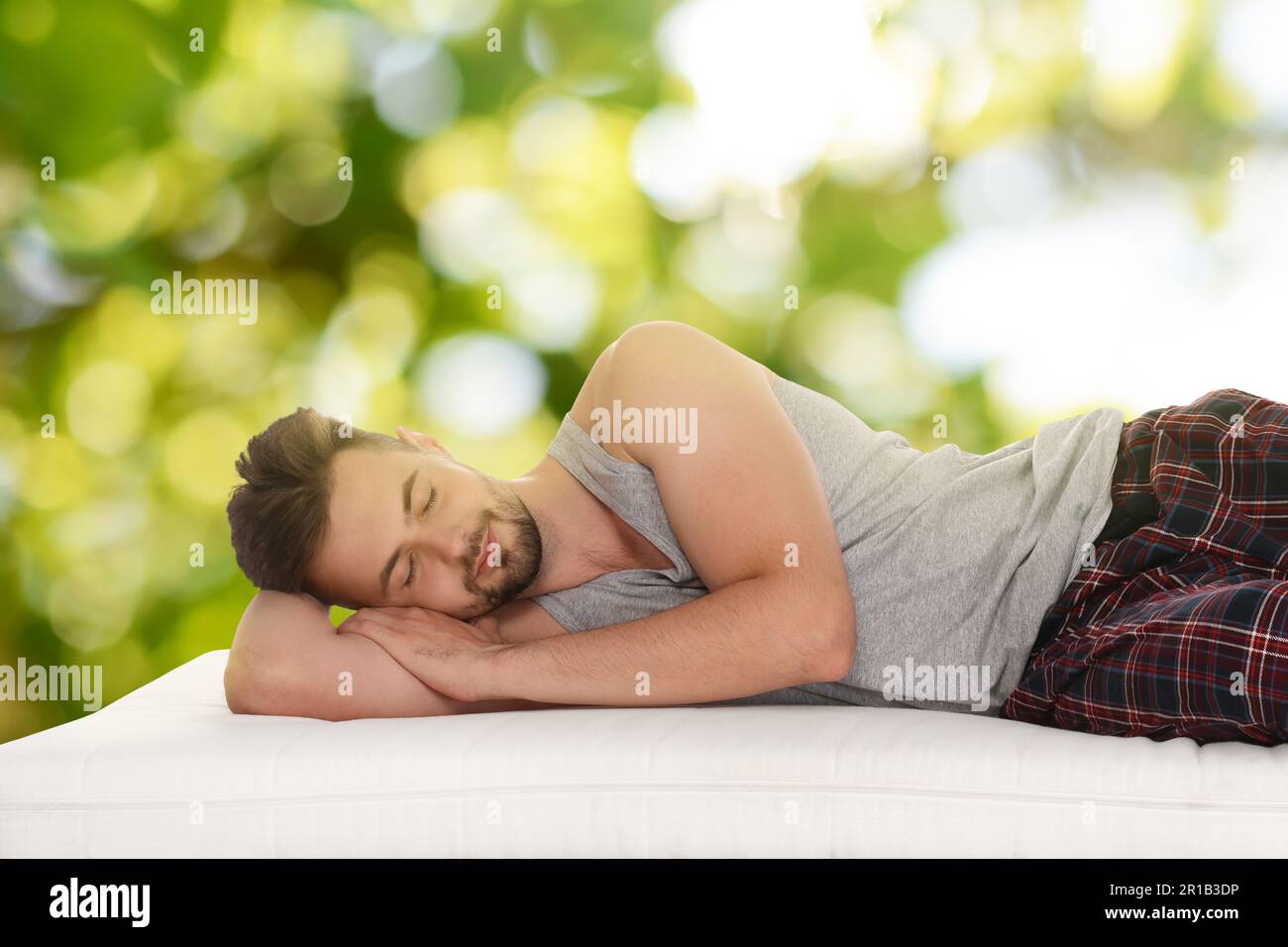 Uomo che dorme su un comodo materasso su sfondo verde sfocato, effetto bokeh. Dormi bene - resta in salute Foto Stock