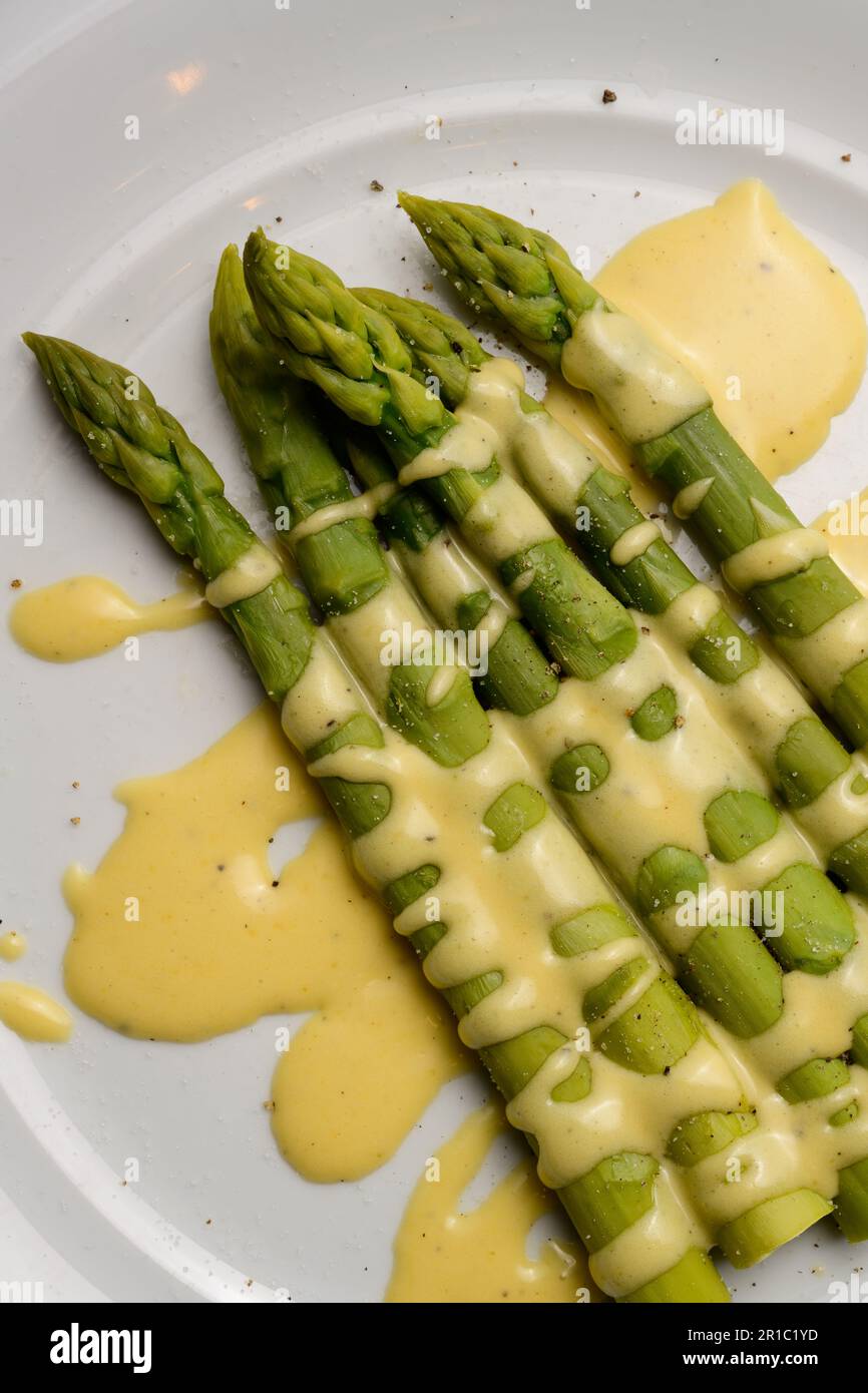 Asparagi verdi con salsa olandese serviti su un piatto bianco Foto Stock