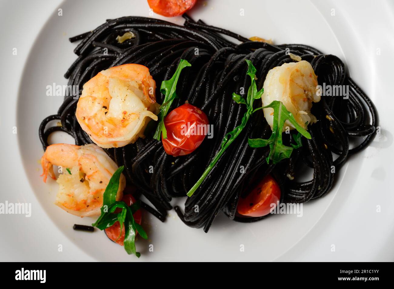 Spaghetti al Nero di Seppia con Gamberi, Pasta italiana con inchiostro calamaro, gamberi, pomodoro e rucola Foto Stock