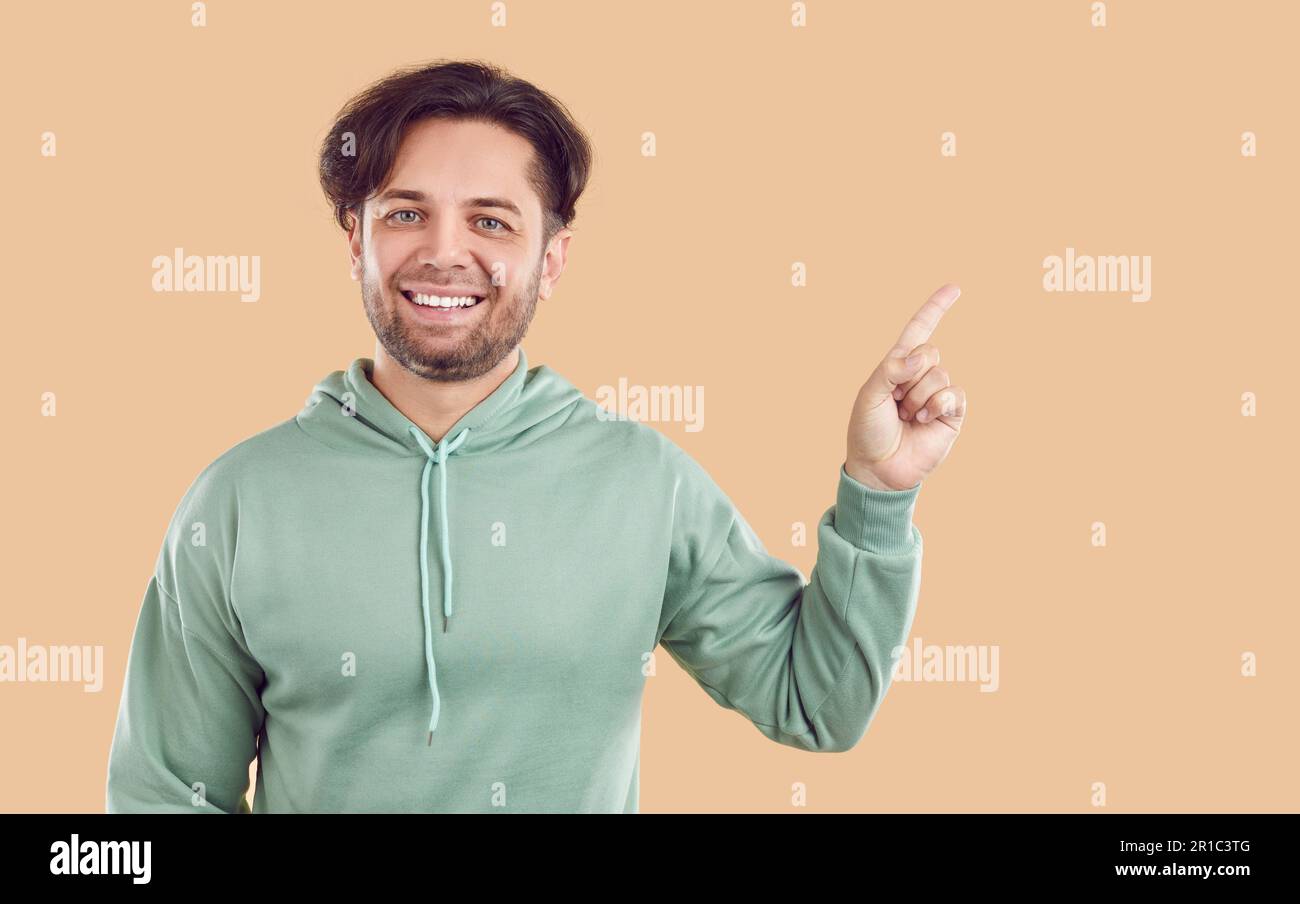Sorridente ridendo felice uomo bearded sta puntando il dito indice sullo spazio della copia su sfondo beige. Foto Stock