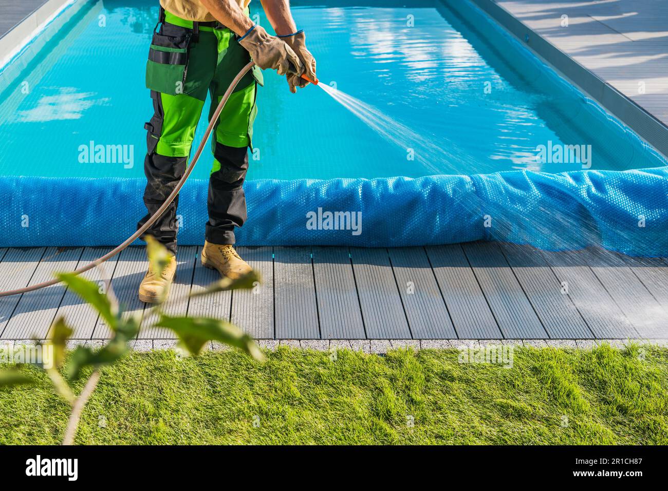 Prendersi cura di un cortile a bordo piscina. Proprietario del giardino pulizia della piattaforma della piscina usando il tubo dell'acqua Foto Stock