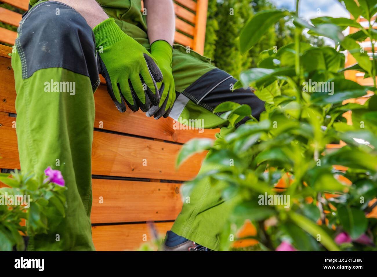 Pausa lavoro manutenzione giardino primavera. Uomo caucasico rilassante mentre si sida su una piantatrice di legno. Foto Stock