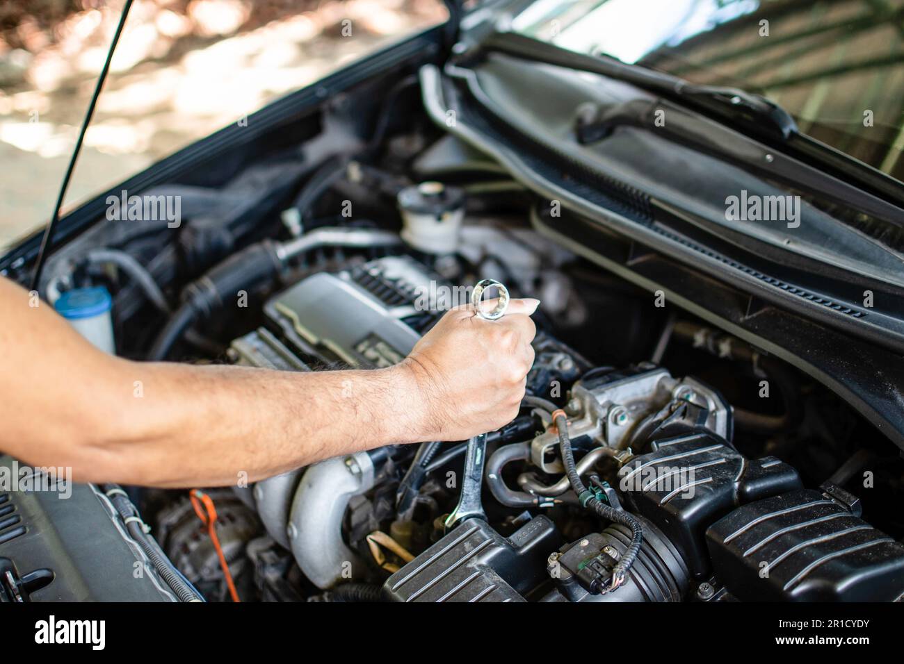 Concetto di manutenzione del motore. I meccanici tengono una chiave per serrare i bulloni durante le riparazioni del motore. Auto nera, motore spento. Gli ingegneri stanno controllando il co Foto Stock