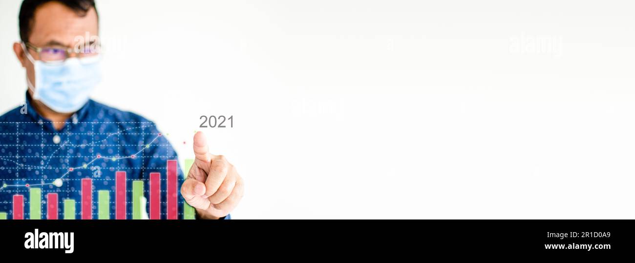 Primo piano, uomo d'affari che indossa una maschera di coronavirus, o COVID-19, sta puntando il dito su un grafico a colori che mostra l'attività di mercato 2021. CopySpace attivato Foto Stock