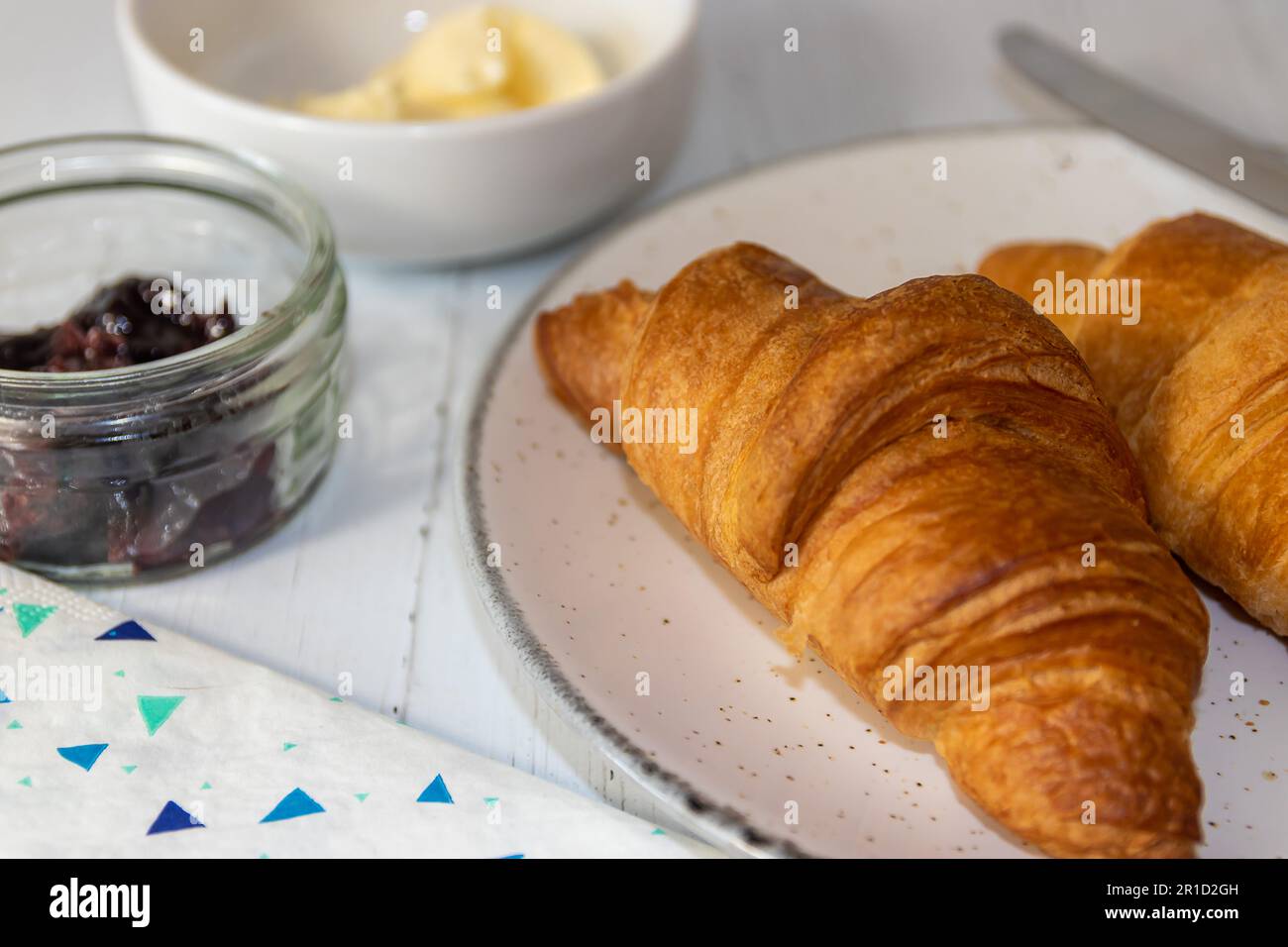 Due croissant con burro e marmellata a lato con coltello sul piatto Foto Stock