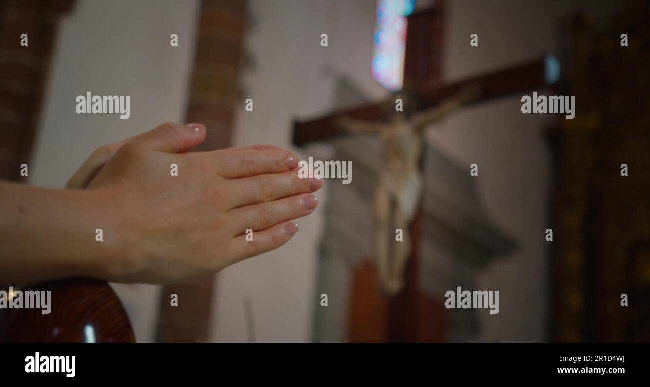 Mani ravvicinate in preghiera contro la croce con Gesù Cristo crocifisso Redentore nella chiesa tradizionale. Foto Stock