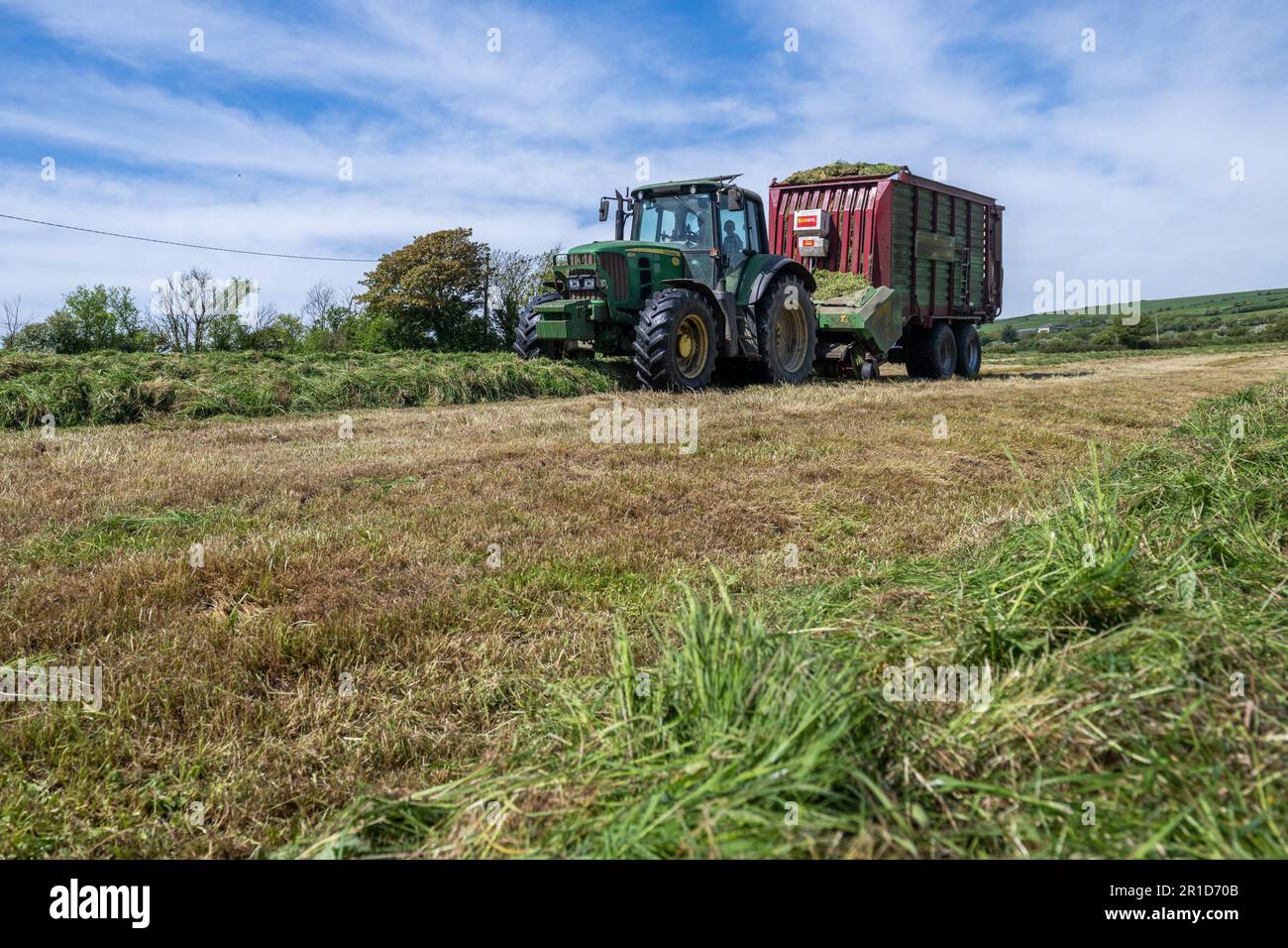 Courtmacsherry, West Cork, Irlanda. 13th maggio, 2023. Matt Hurley raccoglie l'erba per l'insilato utilizzando un trattore John Deere 6930 e un carro per insilato in una calda giornata di sole a West Cork. Met Éireann ha previsto temperature fino a raggiungere i 20C°C nei prossimi giorni prima che la pioggia si stabilirà nella prossima settimana. Credit: AG News/Alamy Live News Foto Stock