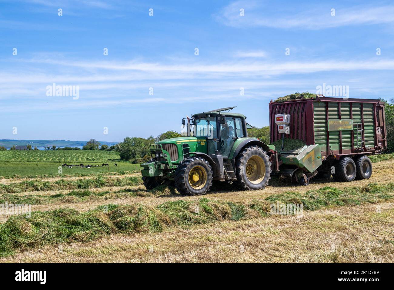 Courtmacsherry, West Cork, Irlanda. 13th maggio, 2023. Matt Hurley raccoglie l'erba per l'insilato utilizzando un trattore John Deere 6930 e un carro per insilato in una calda giornata di sole a West Cork. Met Éireann ha previsto temperature fino a raggiungere i 20C°C nei prossimi giorni prima che la pioggia si stabilirà nella prossima settimana. Credit: AG News/Alamy Live News Foto Stock