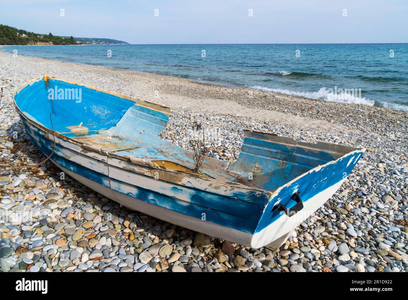 Una barca abbandonata rotta piena di buchi giacenti sulla riva del mare in bassa stagione Foto Stock