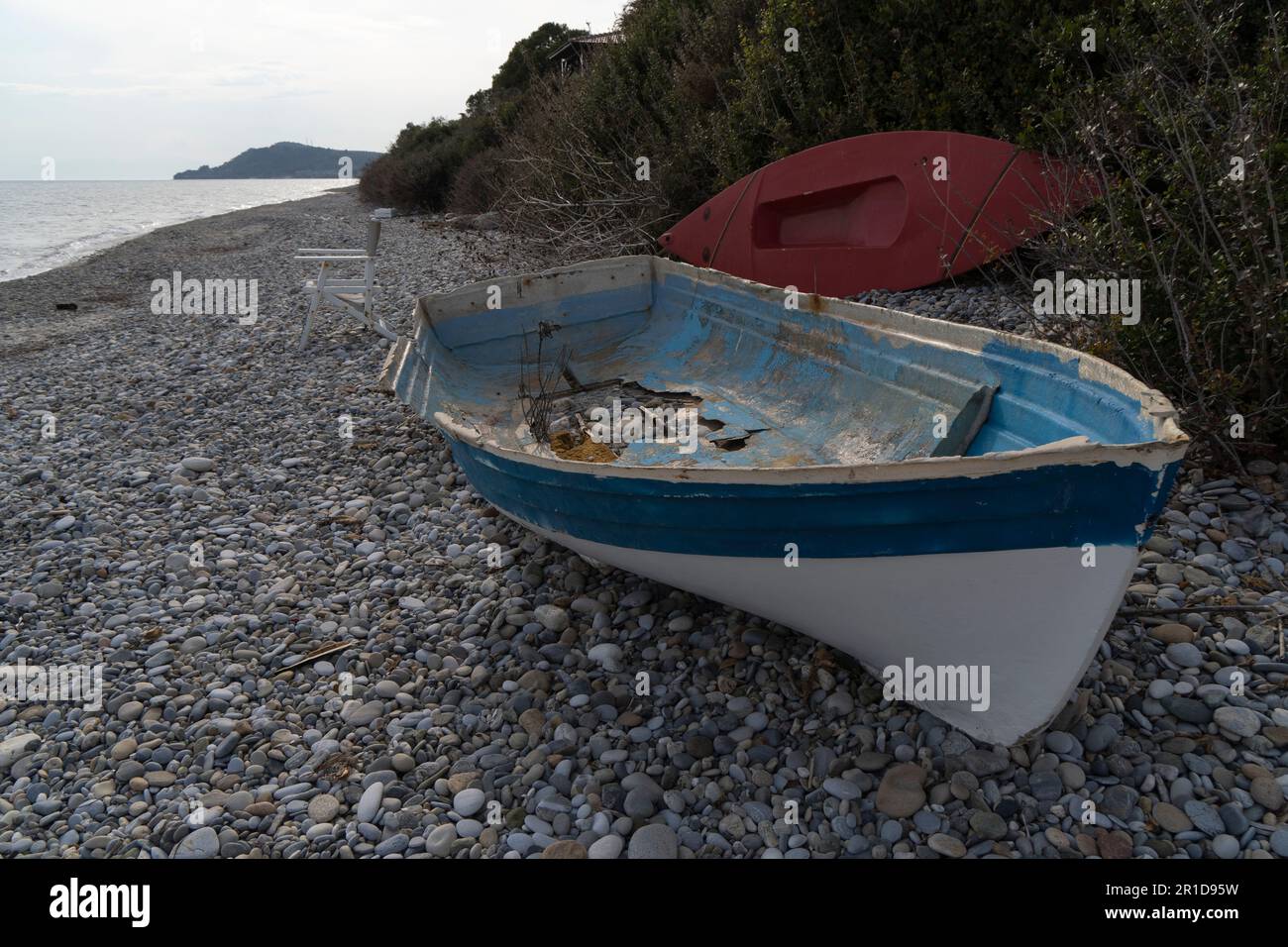 Una barca abbandonata rotta piena di buchi giacenti sulla riva del mare in bassa stagione Foto Stock