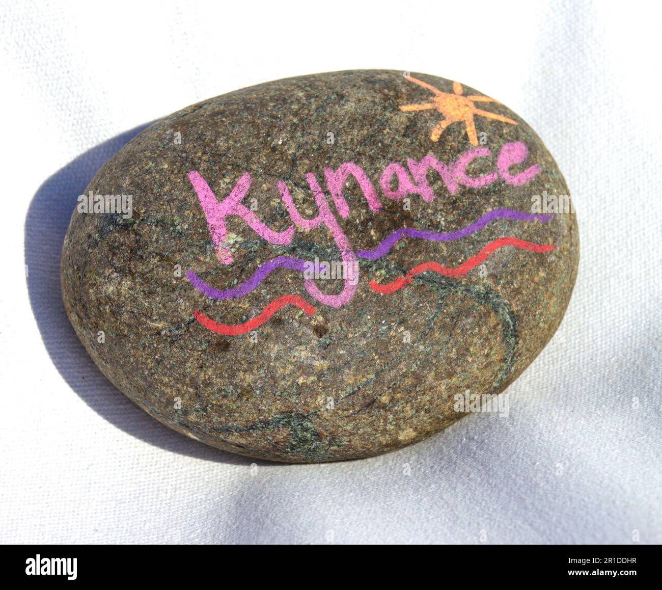 Luminosa pietra da spiaggia dipinta d'estate su una sedia a sdraio in tela bianca. A Kynance Cove sulla Penisola di Lizard, Cornovaglia. Foto Stock