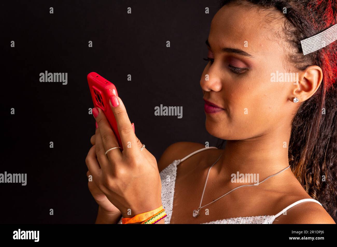 Adolescente, sorridente, concentrato sul telefono cellulare, isolato su sfondo nero. Foto Stock