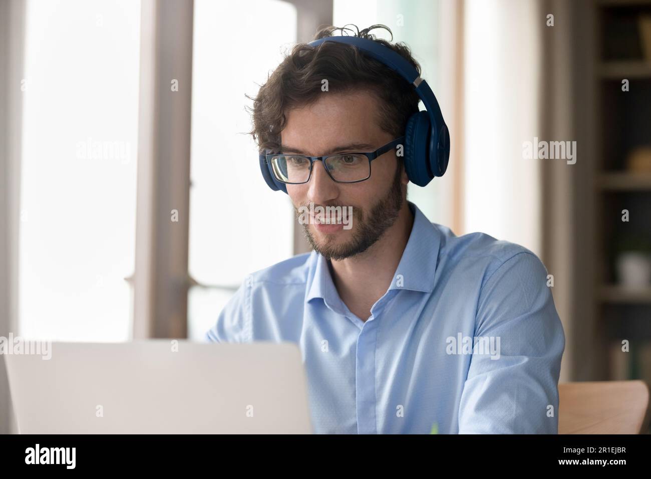 Uomo freelance positivo in occhiali e cuffie che parlano al computer portatile Foto Stock