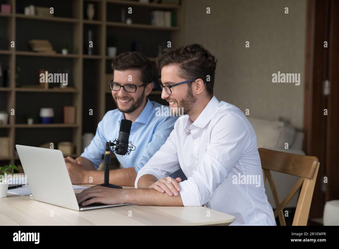 Due allegri uomini seduti al computer portatile e al microfono dello studio Foto Stock