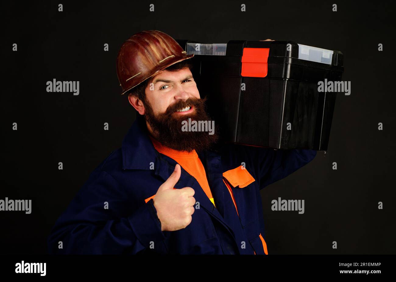 Il costruttore in casco protettivo con cassetta attrezzi mostra il pollice in alto. Attrezzi per la riparazione. Riparatore in uniforme con cassetta attrezzi. Handyman con kit di riparazione. Strumenti Foto Stock