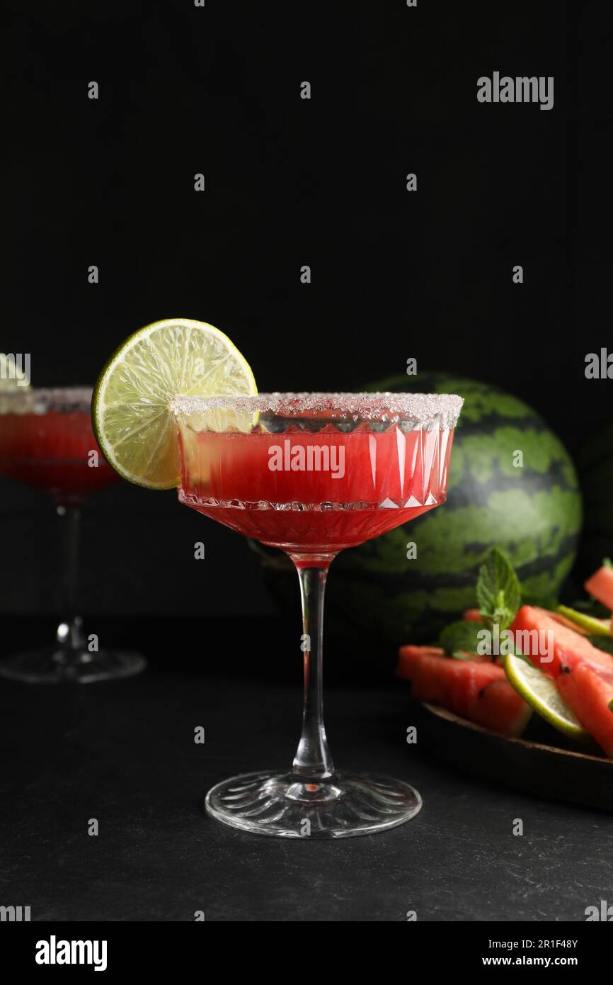 Bicchieri da cocktail di delizioso succo di cocomero fresco con lime e zucchero sul tavolo nero Foto Stock