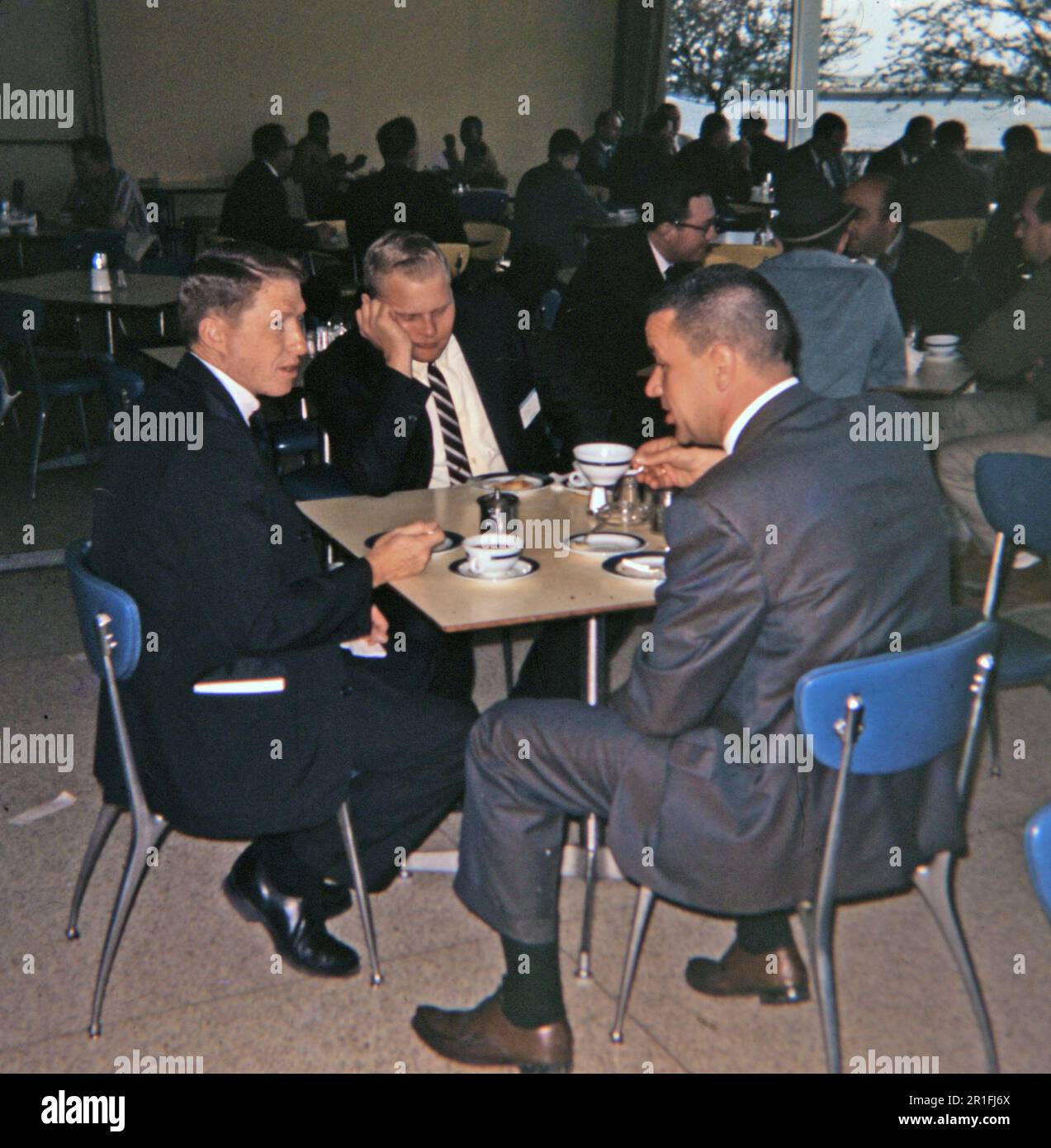 Tre uomini d'affari seduti in un caffè o caffetteria con una conversazione ca. 1960s Foto Stock