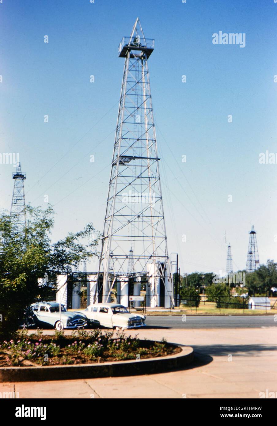 Auto parcheggiate di fronte a un petrolio derrick in Oklahoma (r) ca. 1950-1955 Foto Stock
