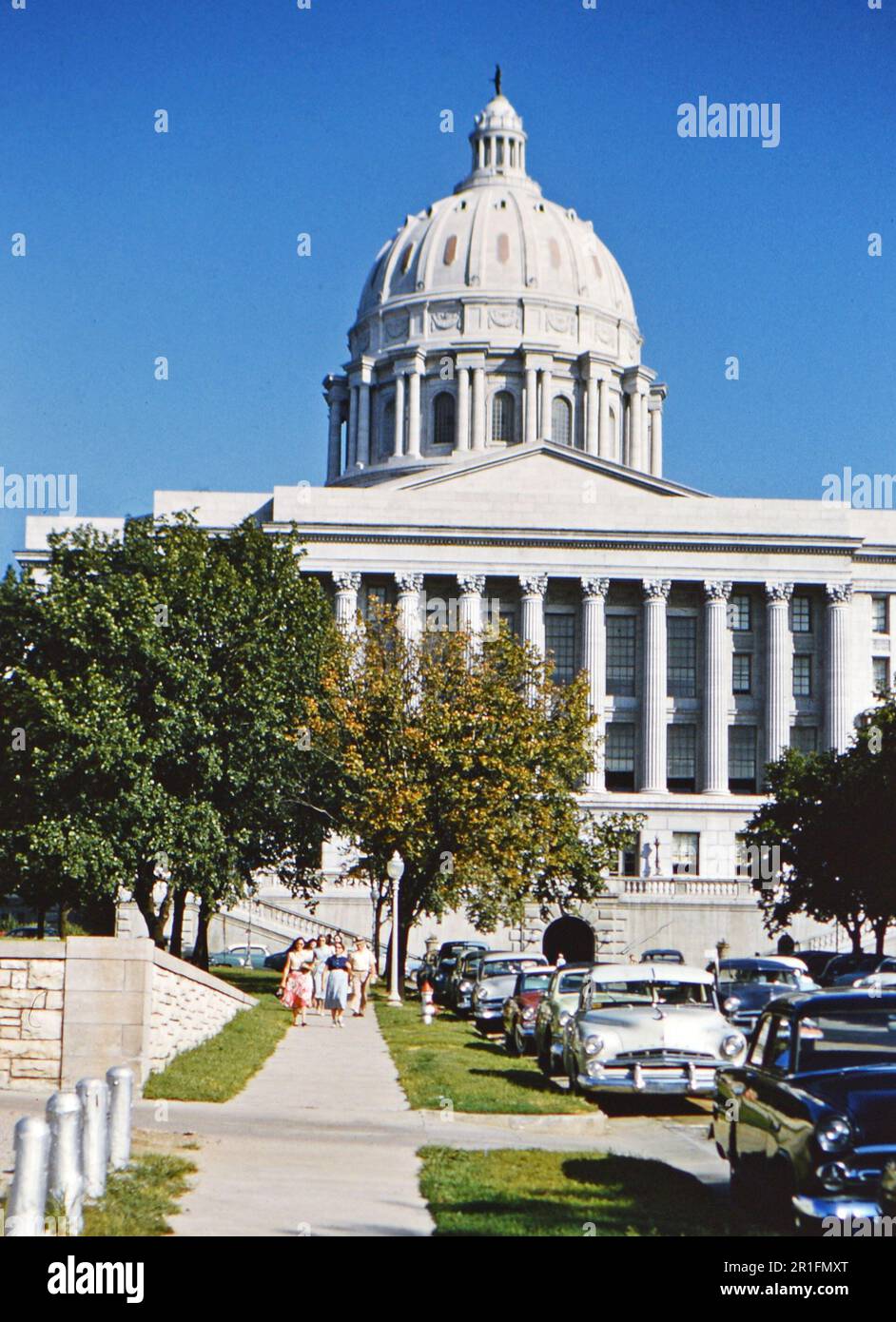 Auto parcheggiate lungo una strada di fronte al campidoglio dello stato del Missouri a Jefferson City, Missouri. Un gruppo di donne e uomini che camminano sul marciapiede che conduce dall'edificio del campidoglio (r) ca. 1950-1955 Foto Stock