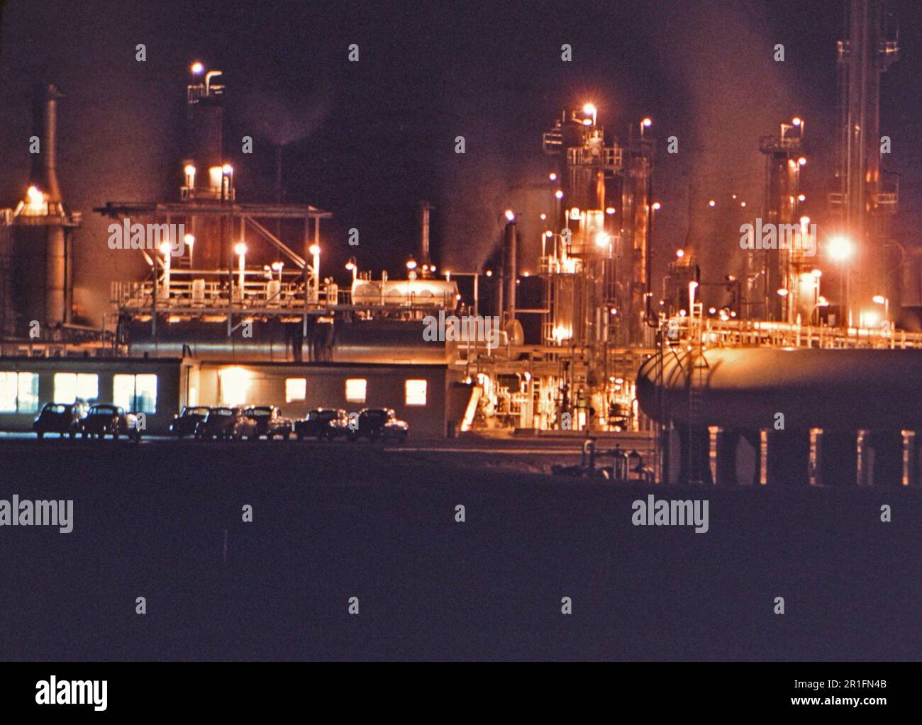 Auto parcheggiate di fronte ad una raffineria di petrolio di notte ca. 1956 Foto Stock