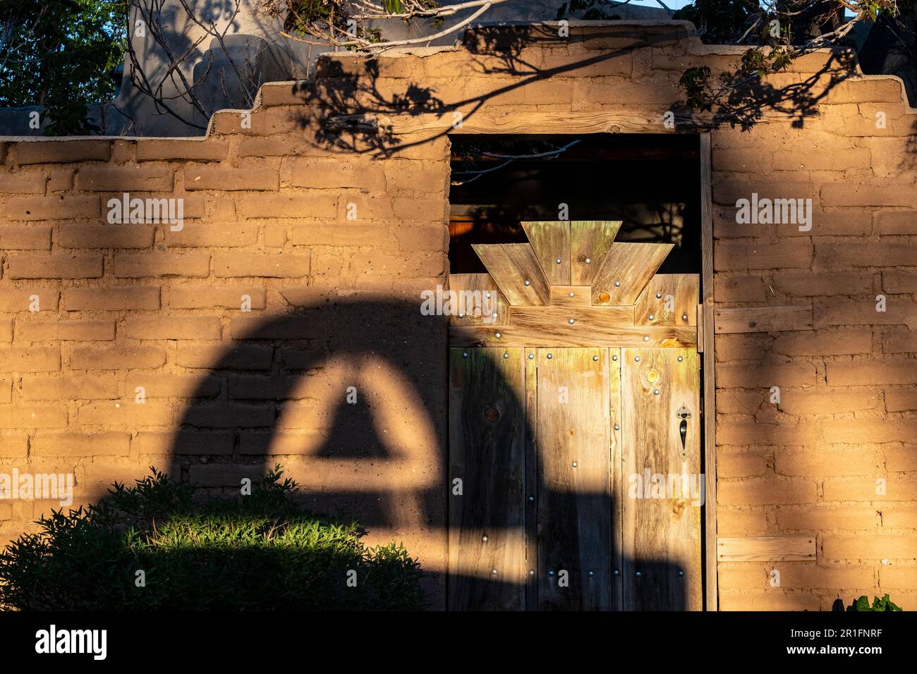 Cerrillos, New Mexico, USA -- un campanile proietta un'ombra al tramonto contro una porta di legno e muro di adobe Foto Stock