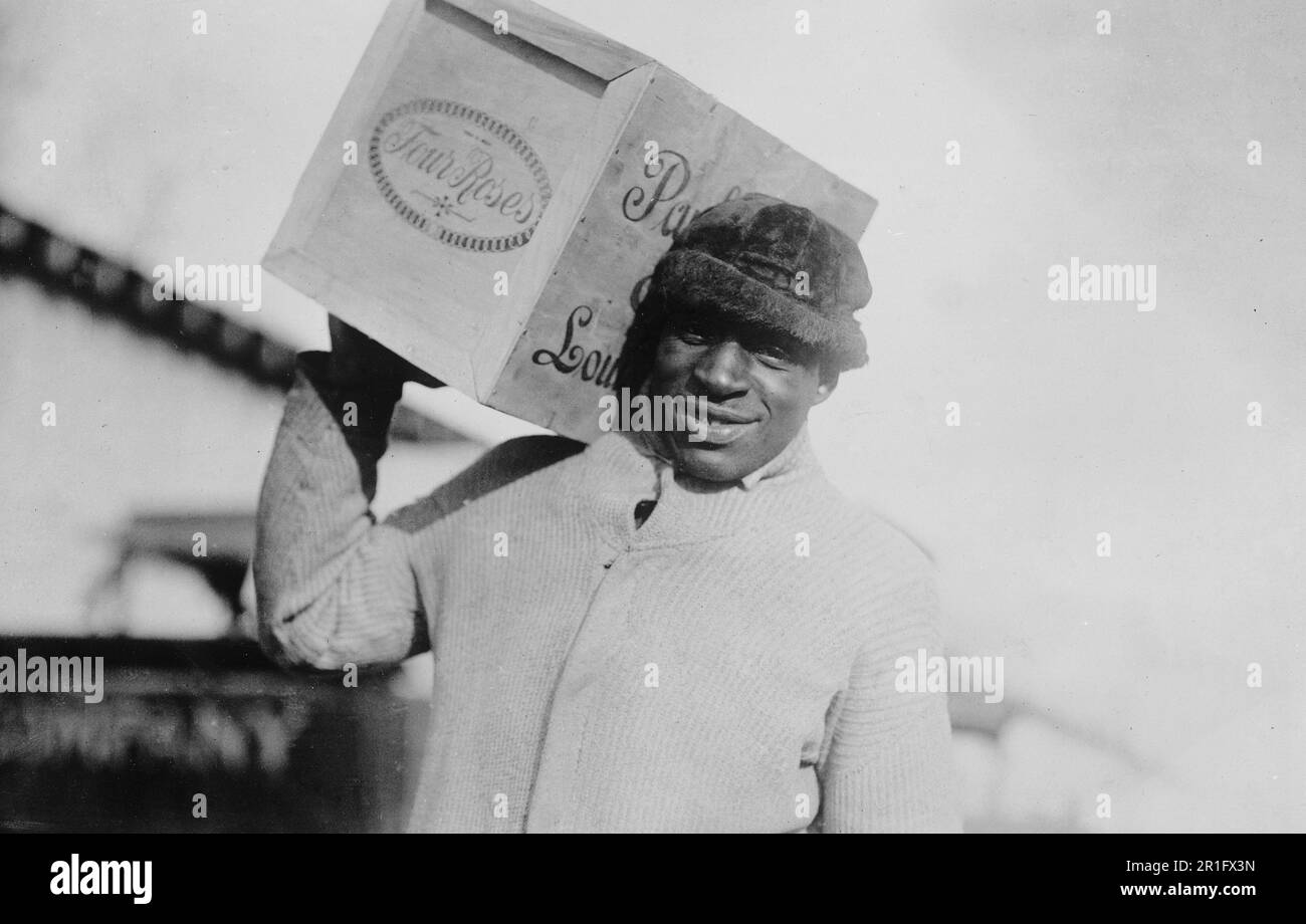 Foto di archivio: Uomo afroamericano che porta un caso di whiskey 'Four Roses' sulla sua spalla, forse confiscato dagli Stati Uniti Internal Revenue Bureau ca. 1921 Foto Stock