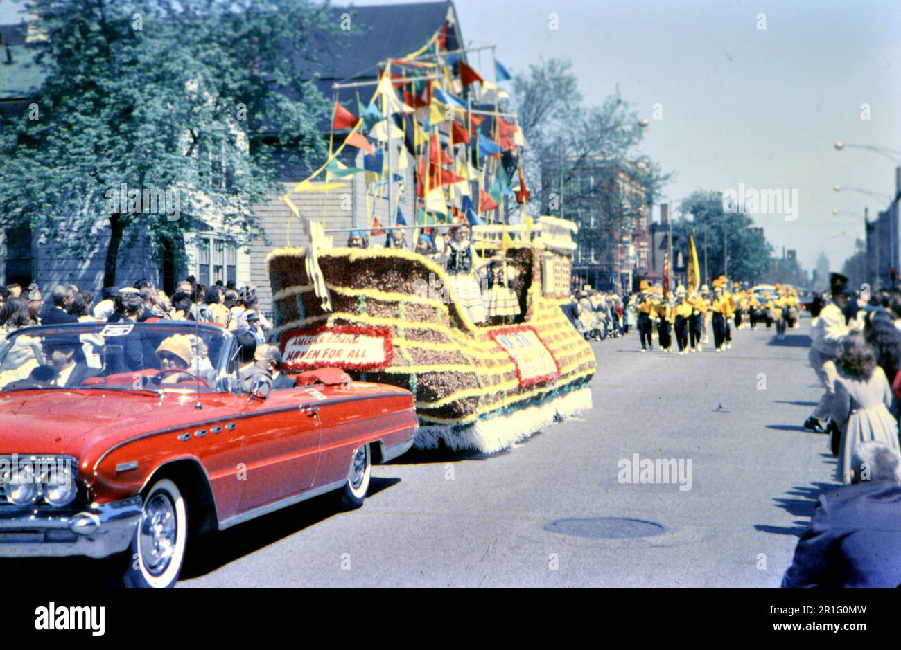 Persone che guardano una parata, un galleggiante che viene tirato da una rossa convertibile ca. 1960s Foto Stock