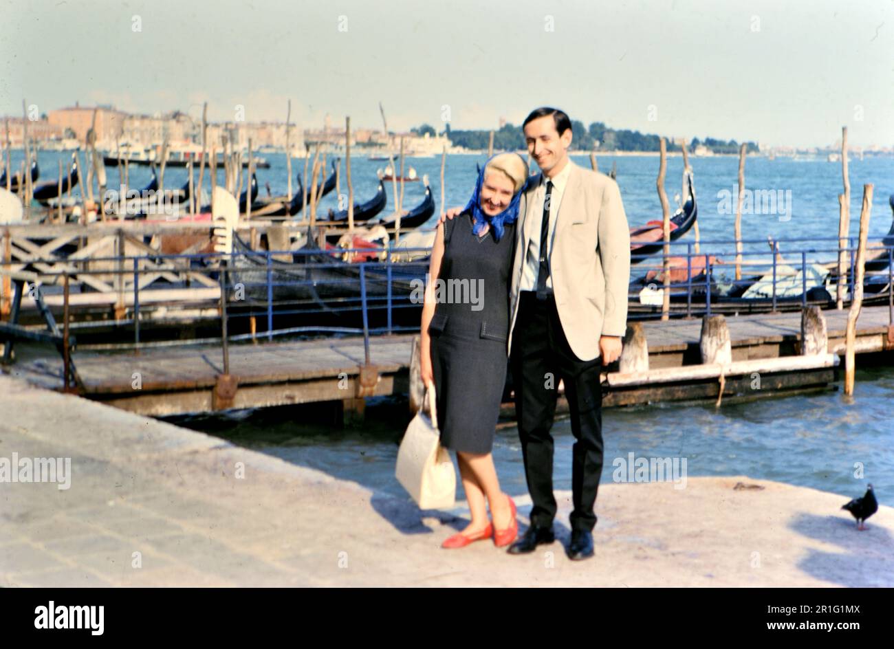 Marito e moglie posano per una fotografia di fronte alle gondole a Venezia mentre sono in vacanza (r) ca. 1966-1972 Foto Stock