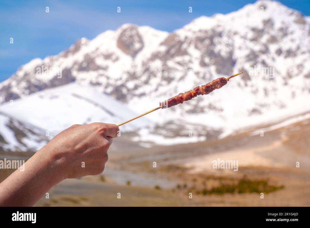 Stiva Arrosticino - tipico spiedino abruzzese - grigliato con montagne di Gran Sasso in pianura campo Imperatore Foto Stock