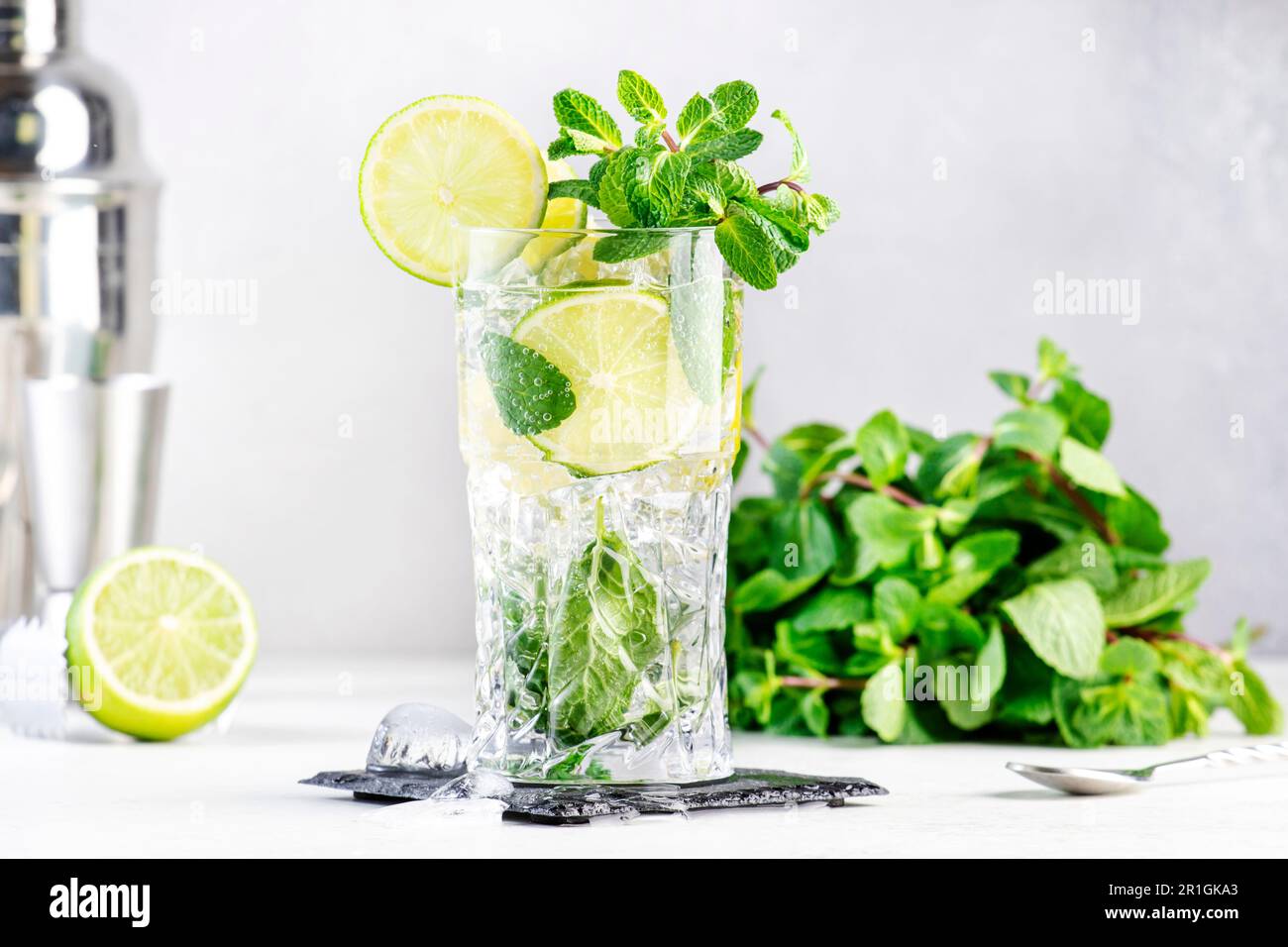 Cocktail estivo Mojito con lime, rum bianco, soda, zucchero di canna, menta,  e ghiaccio in vetro highball su sfondo grigio. Attrezzi per barre in  acciaio. C Foto stock - Alamy