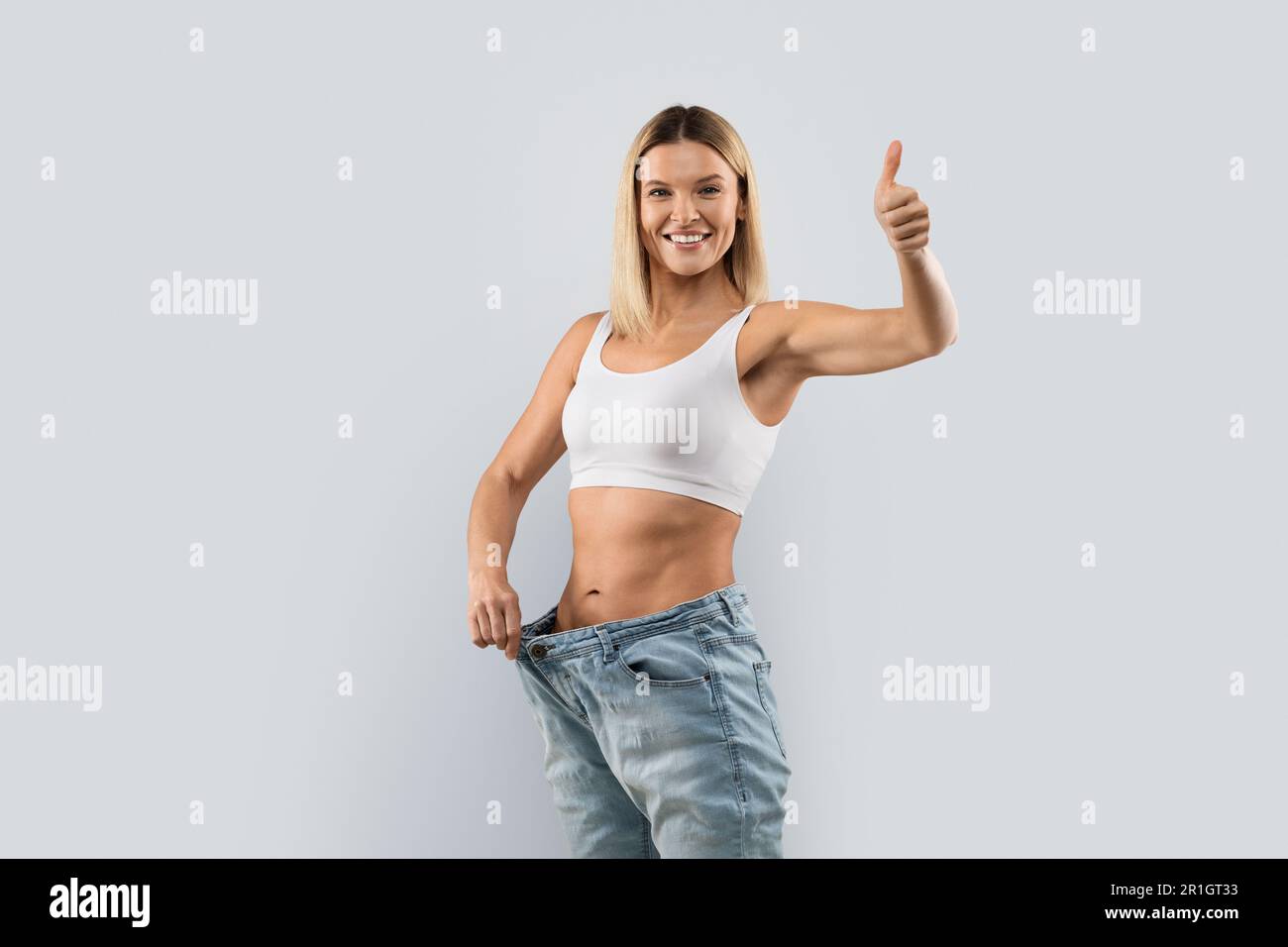 Donna felice di mezza età che indossa jeans grandi mostrando pollice in su Foto Stock