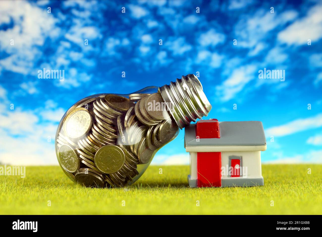 Monete all'interno della lampadina e casa in miniatura sull'erba. Eco-verde energia rinnovabile concetto. I prezzi dell'elettricità, il risparmio energetico in famiglia. Foto Stock