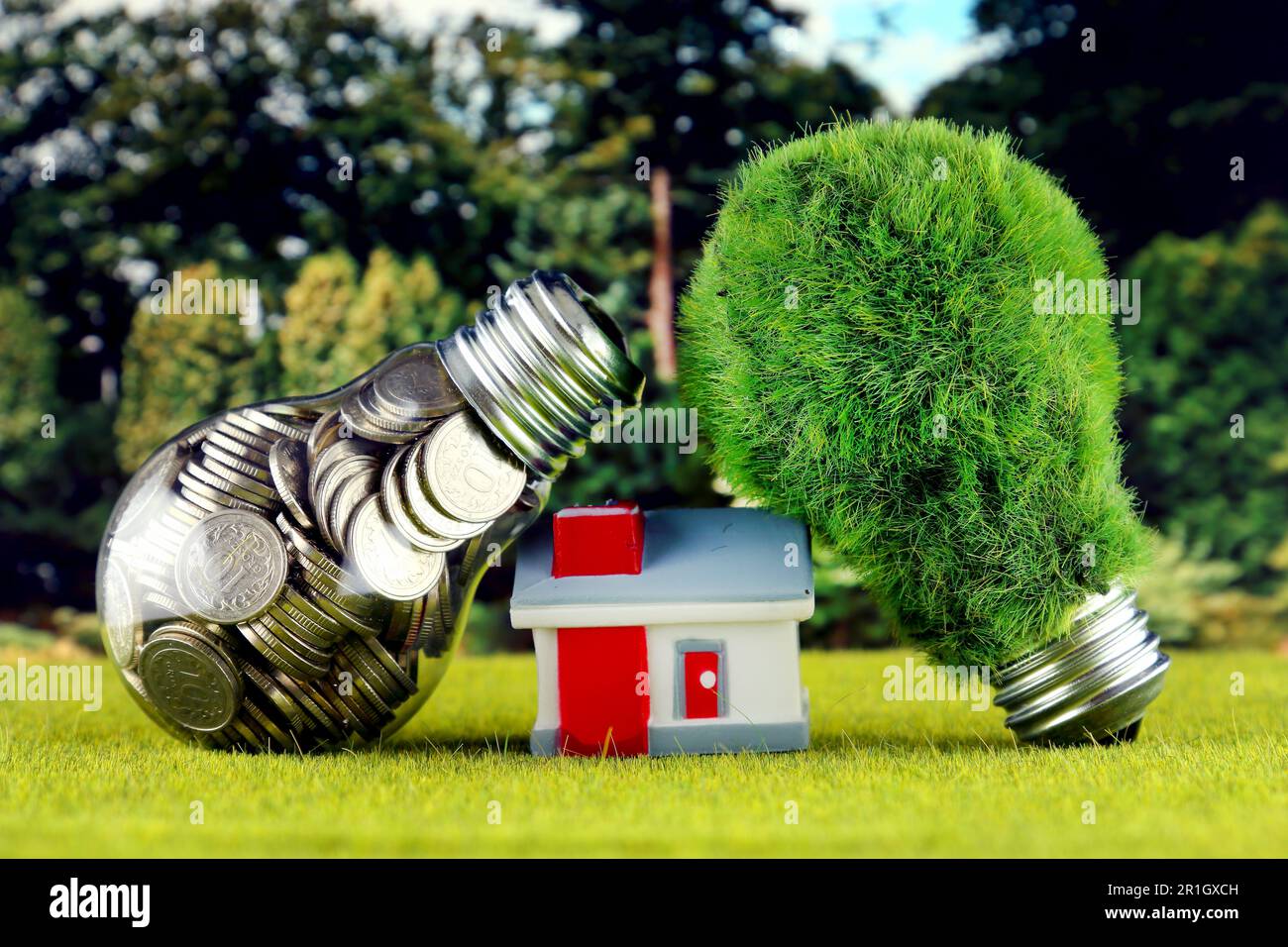 Monete all'interno della lampadina, lampadina verde eco con erba e casa in miniatura. Concetto di energia rinnovabile. I prezzi dell'elettricità, il risparmio energetico nelle ore Foto Stock