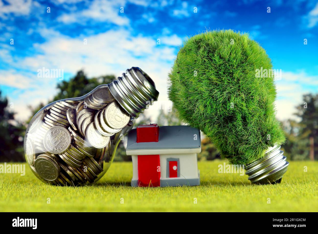 Monete all'interno della lampadina, lampadina verde eco con erba e casa in miniatura. Concetto di energia rinnovabile. I prezzi dell'elettricità, il risparmio energetico nelle ore Foto Stock