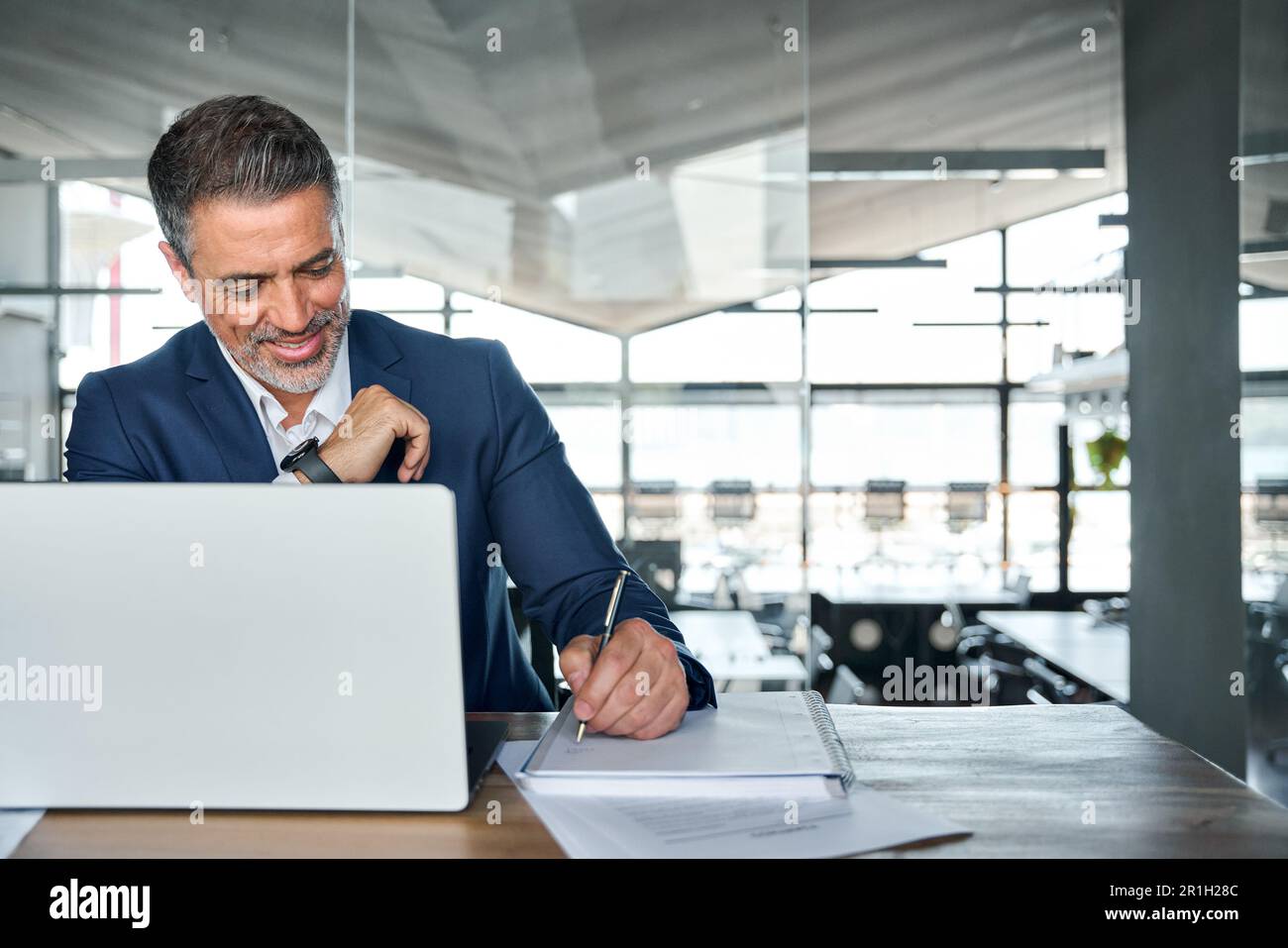 Uomo d'affari anziano impegnato che lavora su un computer portatile in ufficio scrivendo appunti. Foto Stock