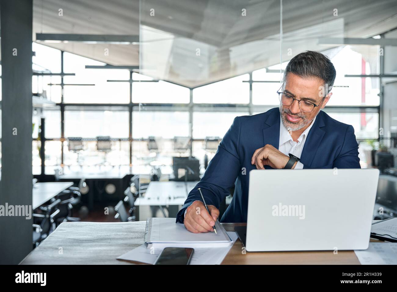 Uomo d'affari di mezza età che lavora su un computer portatile in ufficio scrivendo appunti. Foto Stock