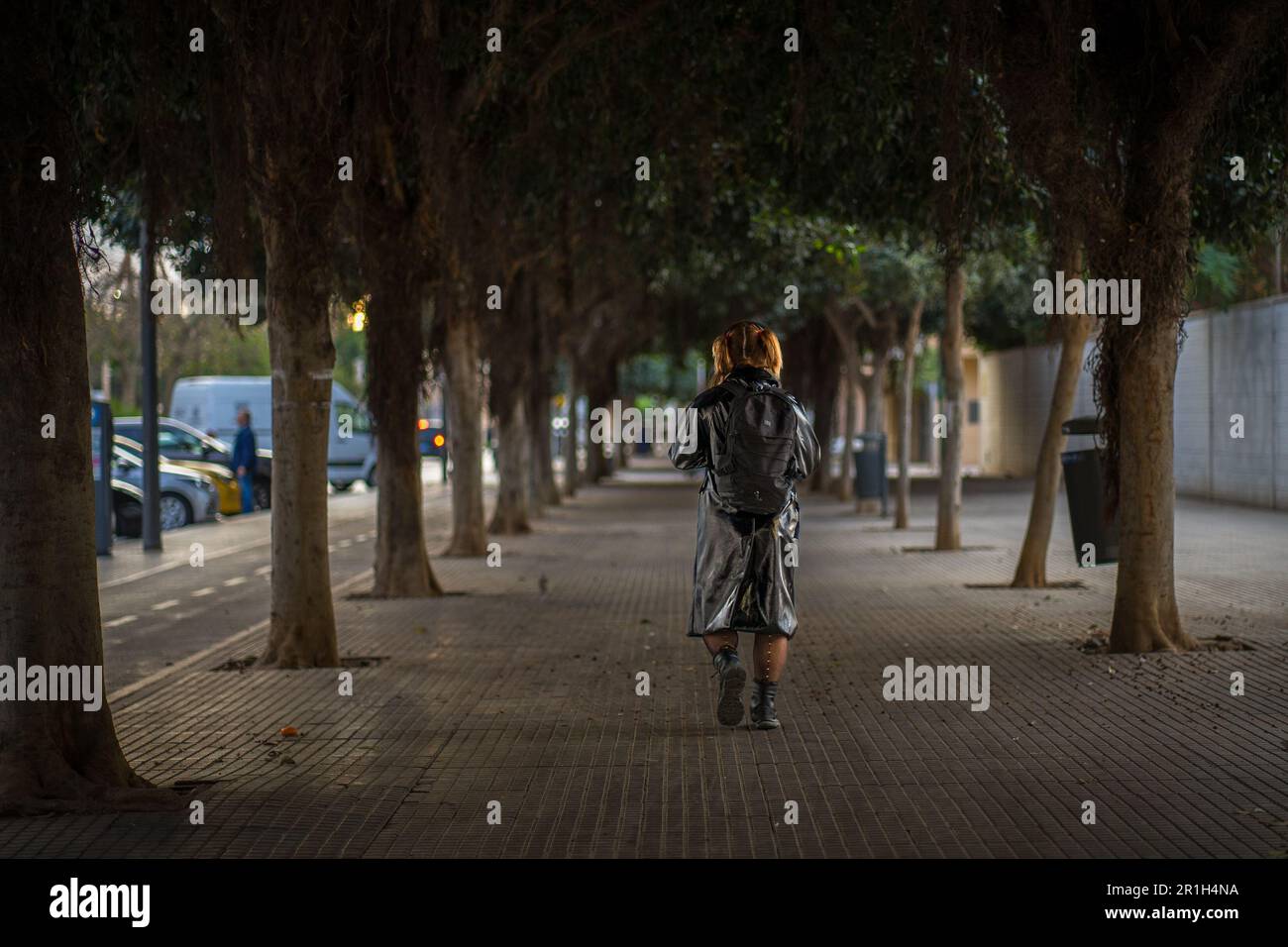 Málaga, Spagna - novembre 25 2022: Ragazza rossa che cammina per strada in abiti neri in stile rocker sotto gli alberi in una passeggiata di Málaga, sparata da dietro Foto Stock