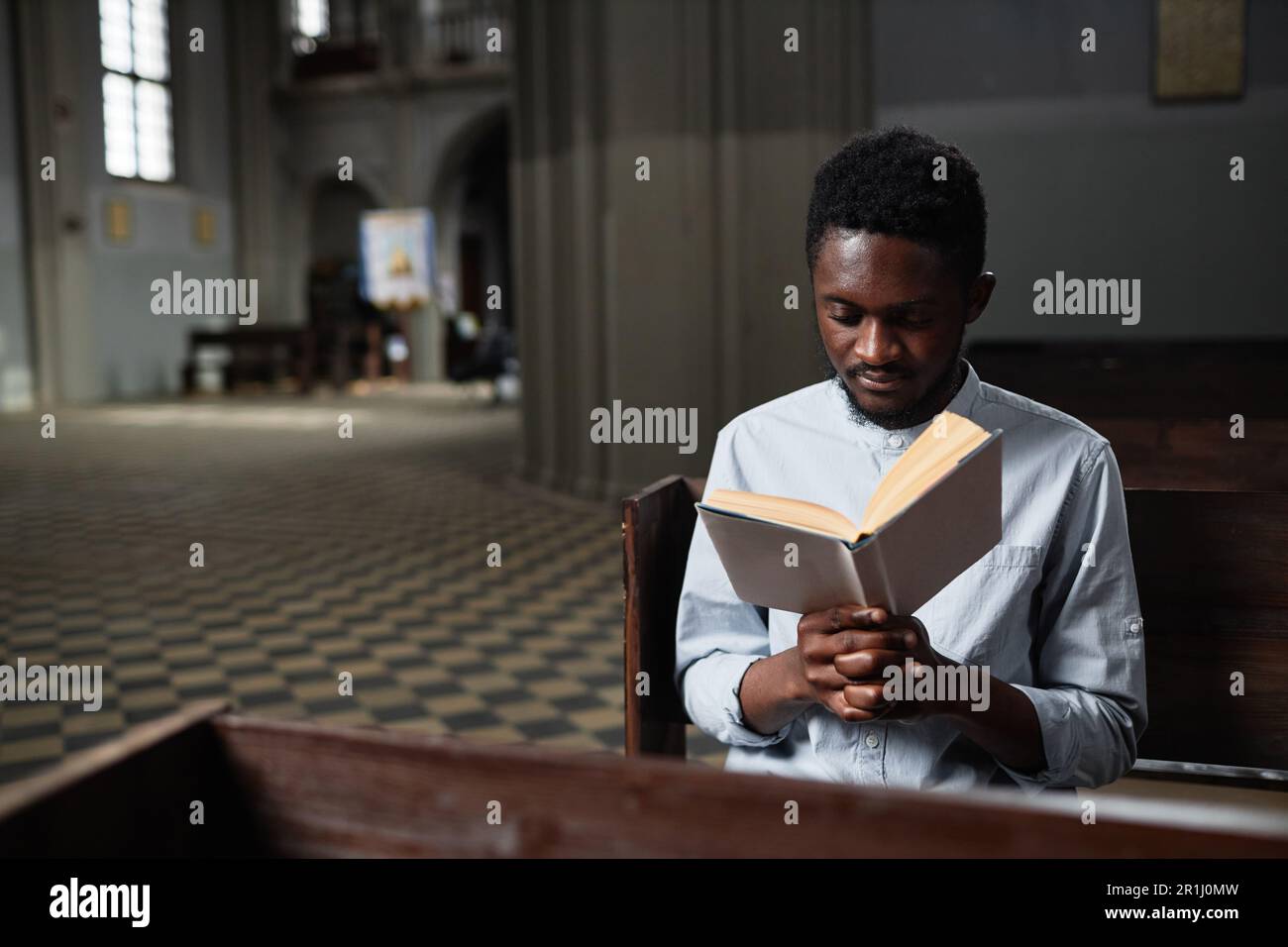 Giovane afro-americano seduto su panchina in chiesa e la preghiera di lettura Foto Stock