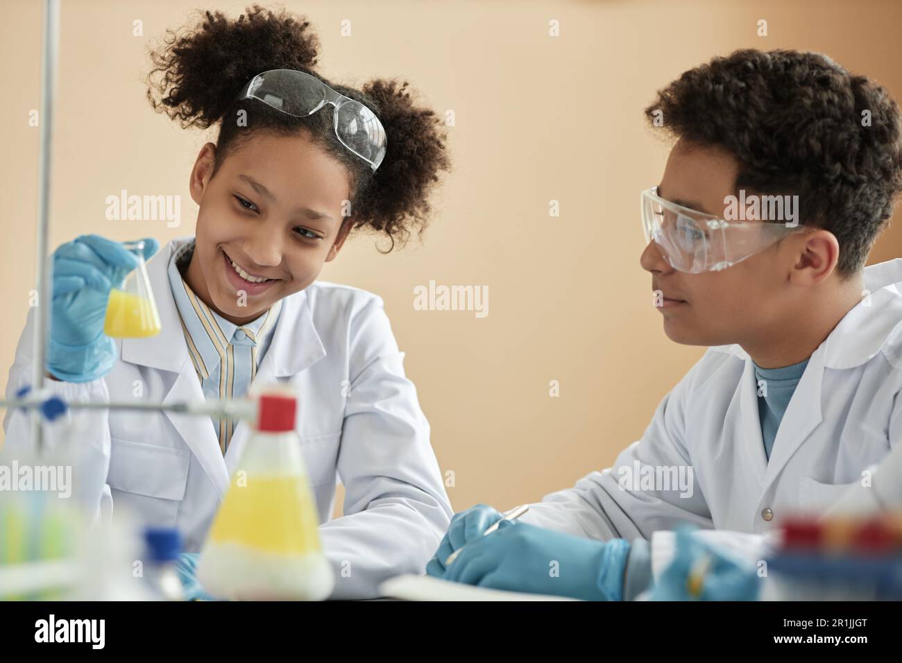 Ritratto di una ragazza nera sorridente che si diverse a scuola e a guardare la reazione chimica Foto Stock
