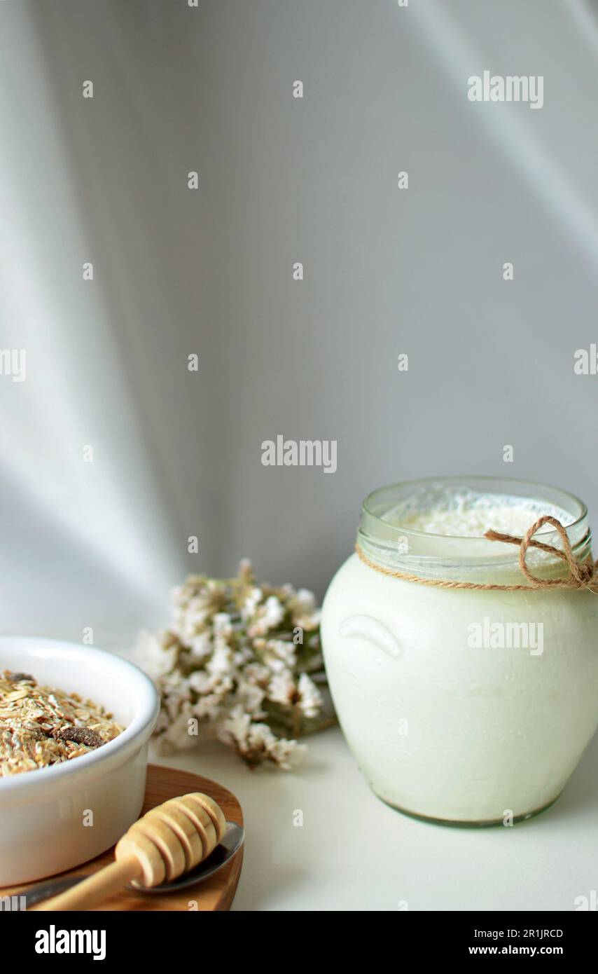 Sul tavolo c'è un vaso di vetro con yogurt bianco fatto in casa. C'è un fiore bianco e spighe di mais sul tavolo. Yogurt greco naturale con schiuma di latte. Foto Stock