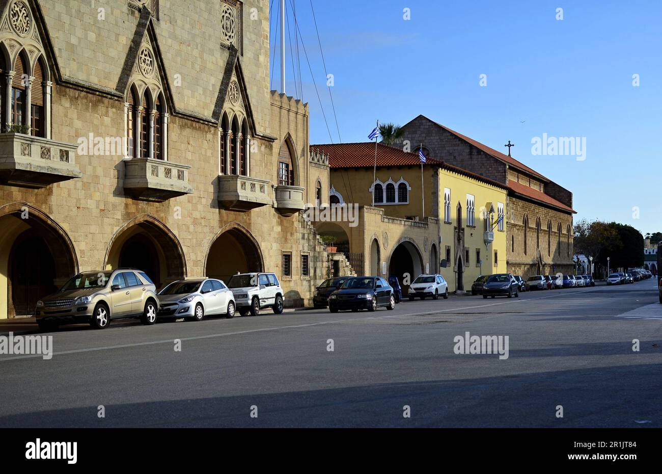 La strada centrale con auto parcheggiate lungo la strada, vicino agli edifici di architettura italiana sull'isola di Rodi, Greece.Mandraki District Foto Stock