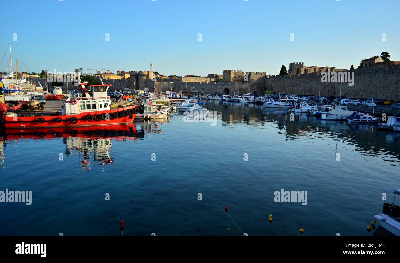 Porto marittimo vicino alle mura della città medievale di Rodi. Barche da pesca, trattori marini e imbarcazioni turistiche sono ormeggiate nel porto Foto Stock