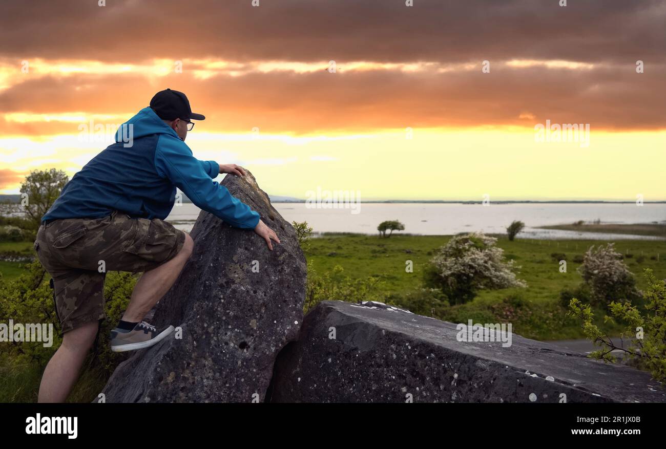 Uomo che si arrampica sulla roccia sulla cima di una collina verde con vista mozzafiato sul lago Corrib a Galway, Irlanda Foto Stock