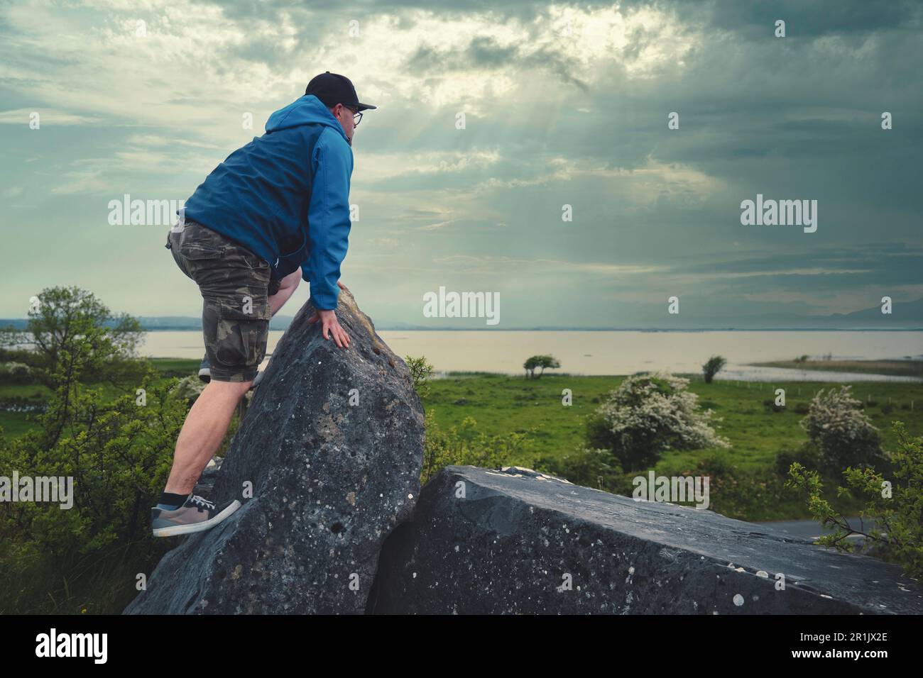 Uomo che si arrampica sulla roccia sulla cima di una collina verde con vista mozzafiato sul lago Corrib a Galway, Irlanda Foto Stock