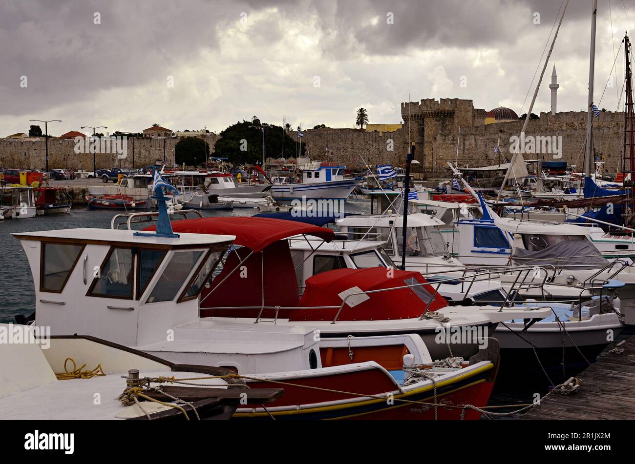 Porto marittimo con barche da pesca e da diporto ormeggiate alle mura della città medievale di Rodi. Barche con tende rosse e bianche. Foto Stock