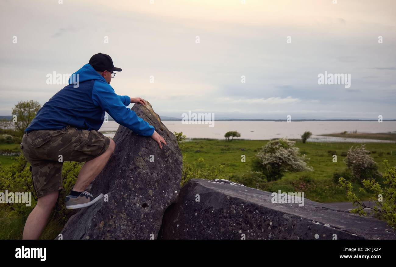Uomo che si arrampica sulla roccia sulla cima di una collina verde con vista mozzafiato sul lago Corrib a Galway, Irlanda Foto Stock