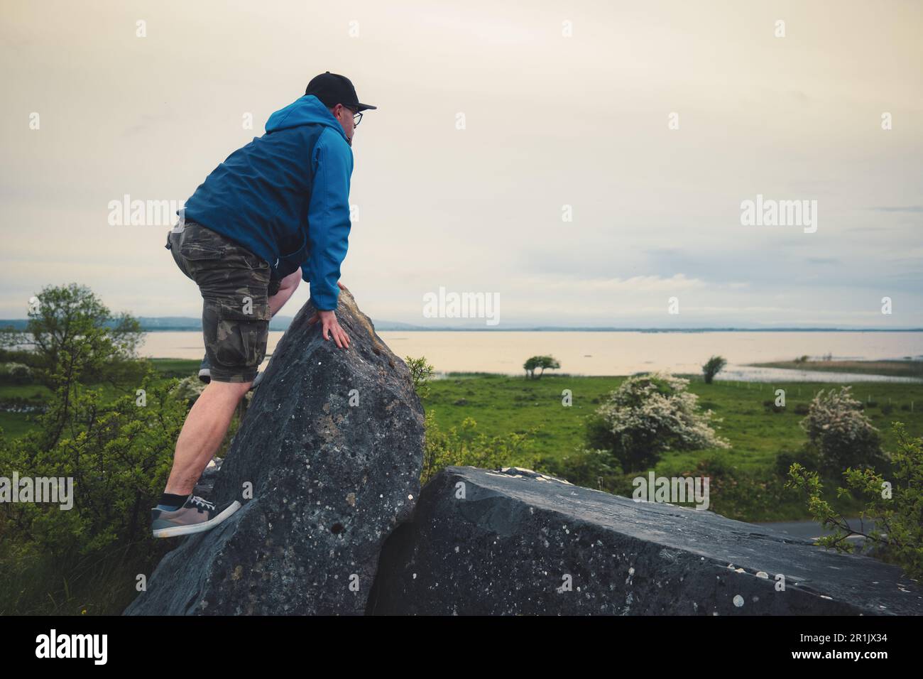 Uomo che si arrampica sulla roccia sulla cima di una collina verde con vista mozzafiato sul lago Corrib a Galway, Irlanda Foto Stock
